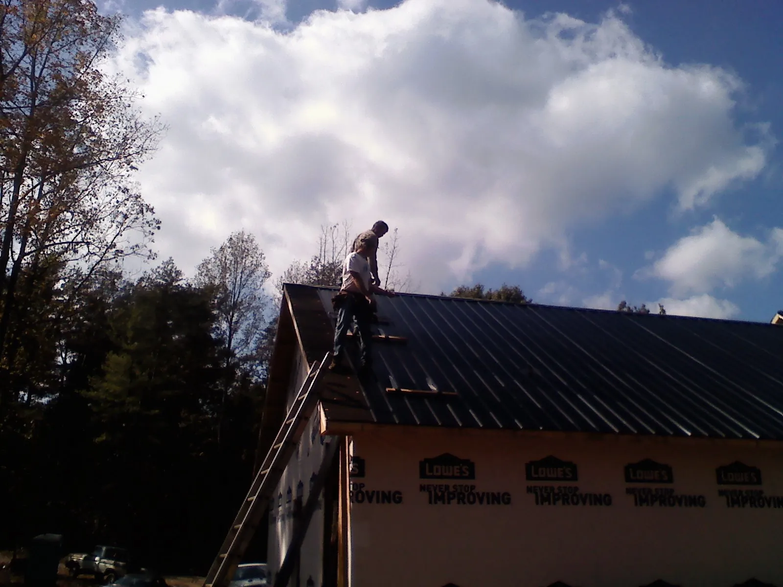 Roofer fastening dark metal panels high against a cloudy sky, from a Roof Inspection job in Dayton